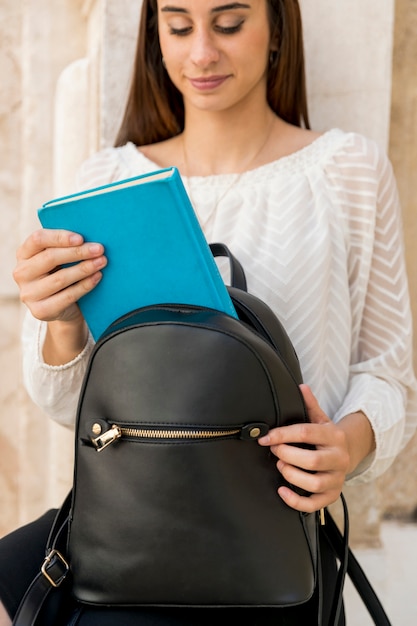 Young brunette putting book in backpack