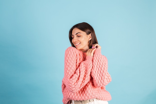 青い壁に分離された暖かいピンクのセーターの若いブルネット