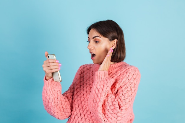 Young brunette in warm pink sweater isolated on blue wall
