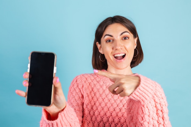 Young brunette in warm pink sweater isolated on blue wall