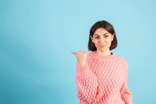 Young brunette in warm pink sweater isolated on blue wall