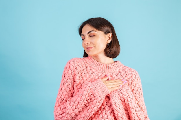 Young brunette in warm pink sweater isolated on blue wall