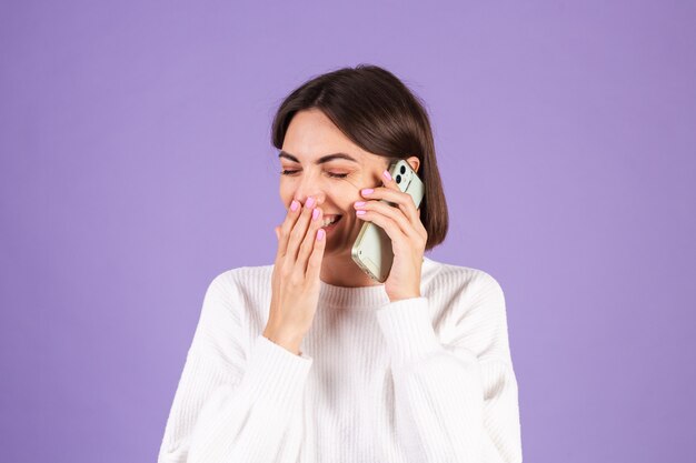 Young brunette in white casual sweater isolated on purple wall