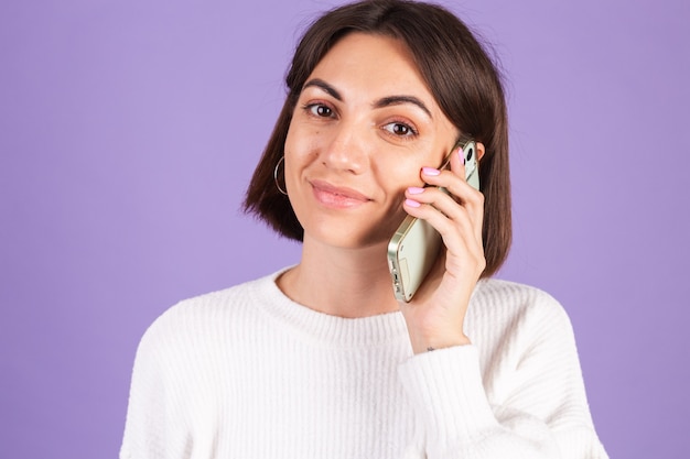 Young brunette in white casual sweater isolated on purple wall