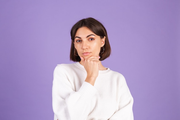 Young brunette in white casual sweater isolated on purple wall