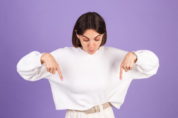 Young brunette in white casual sweater isolated on purple wall