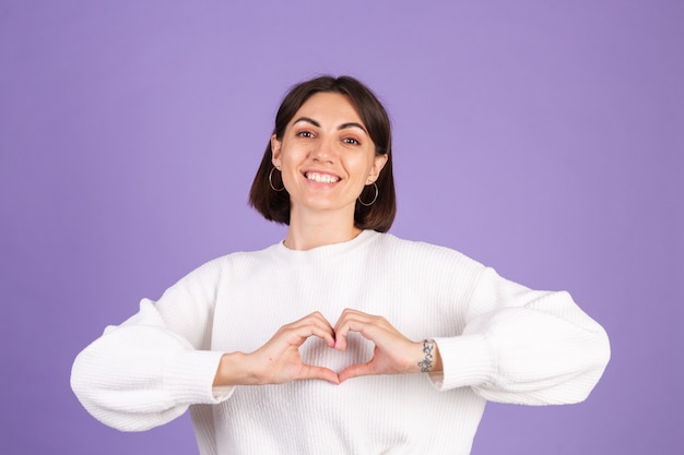 Young brunette in white casual sweater isolated on purple wall