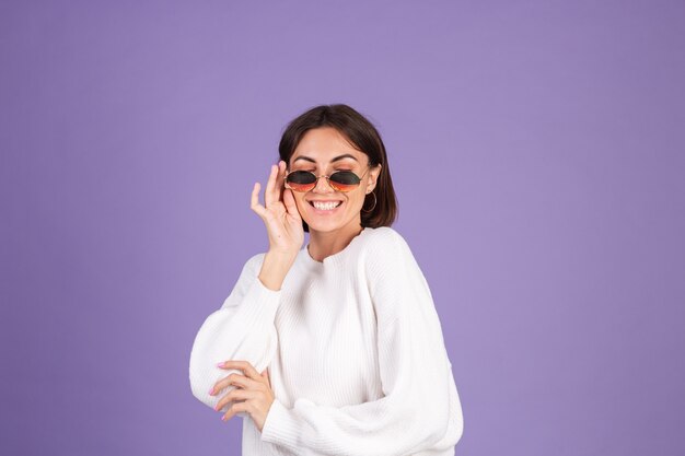 Young brunette in white casual sweater isolated on purple wall