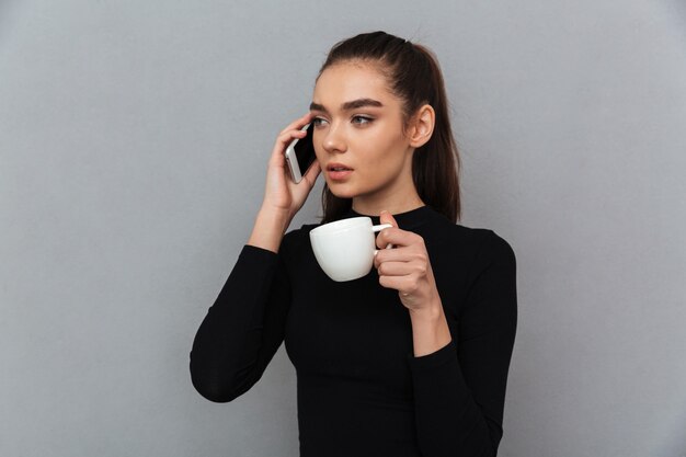 Young brunette woman in black clothes talking by smartphone