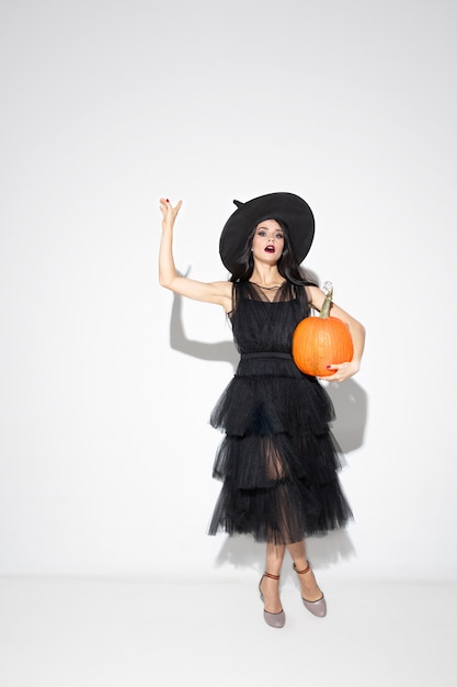 Young brunette woman in black hat and costume on white