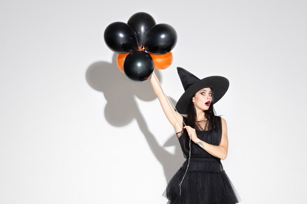 Young brunette woman in black hat and costume on white