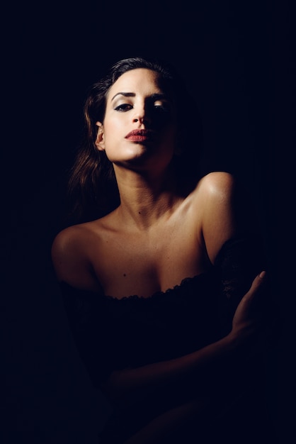 Young brunette woman in black lingerie in chiaroscuro lighting. 