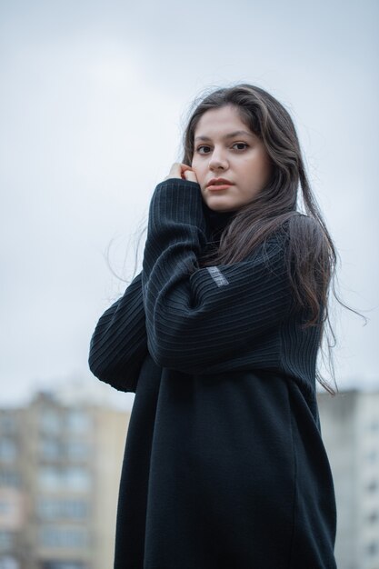 Young brunette woman in black sweater standing on open air