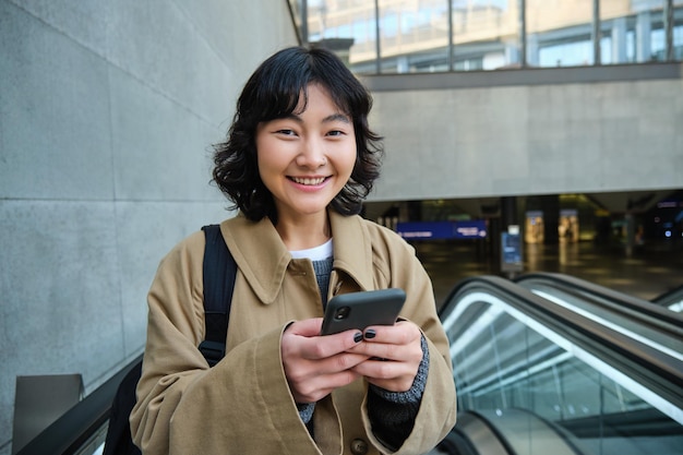 La giovane donna bruna fa il pendolare va da qualche parte in città si trova sulla scala mobile e usa le prese del telefono cellulare