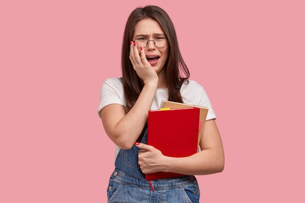 Young brunette woman in denim overalls holding notepads