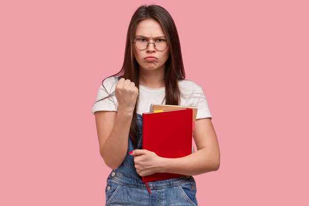 Young brunette woman in denim overalls holding notepads