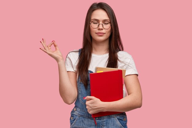 Young brunette woman in denim overalls holding notepads