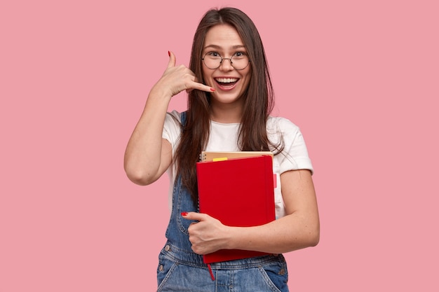 Young brunette woman in denim overalls holding notepads