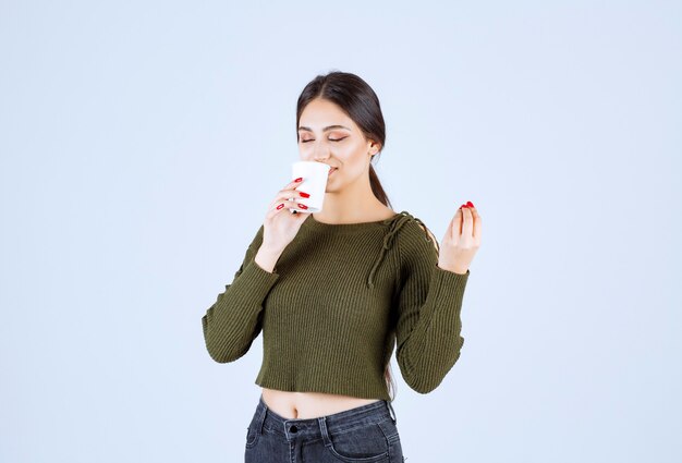 白い背景にお茶のプラスチック カップを飲む若いブルネットの女性。