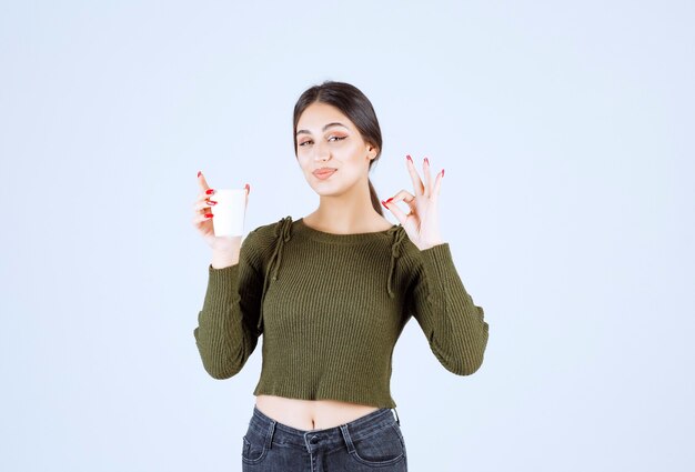 Young brunette woman giving ok sign for tea on white background.