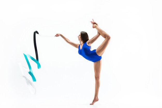 若いブルネットの女性の体操選手は青いリボンでcalilisthenics運動を訓練します