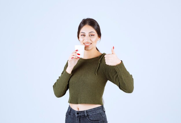 プラスチック カップを押しながら親指をあきらめる若いブルネットの女性。