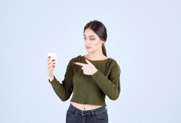 Young brunette woman holding plastic cup happily and pointing at it.