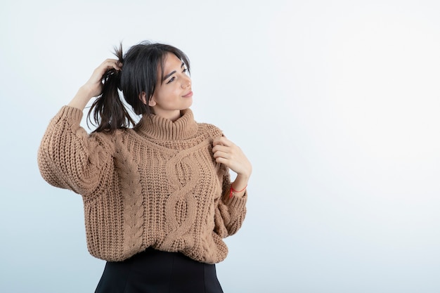 Giovane donna castana in maglieria che tocca i suoi capelli e in piedi