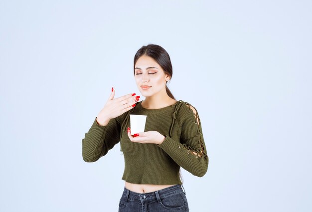 La giovane donna castana odora l'aroma di tè su fondo bianco.