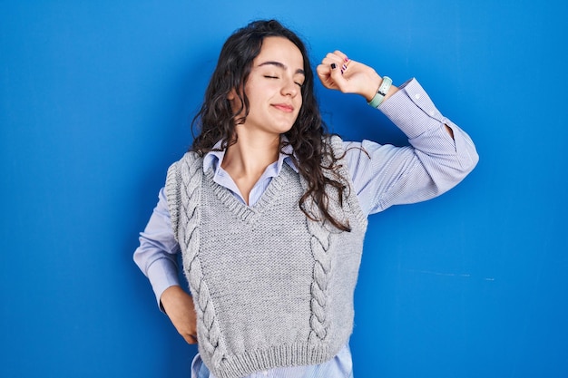 Free photo young brunette woman standing over blue background stretching back, tired and relaxed, sleepy and yawning for early morning