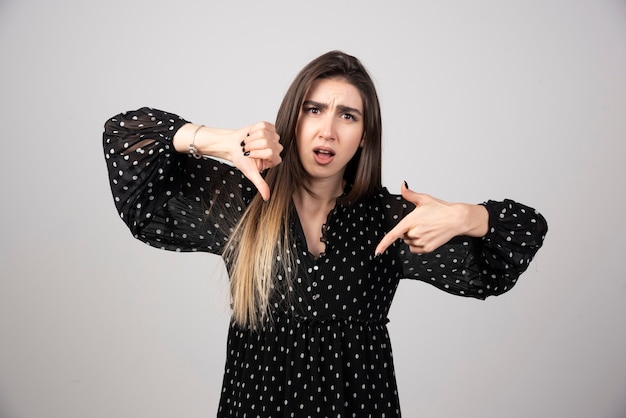 Free photo young brunette woman standing and showing rejection and negative with thumb down gesture.