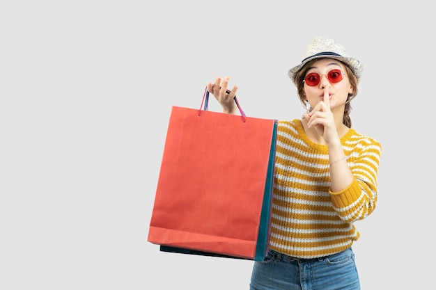 Young brunette woman in sunglasses holding shopping bags and doing silent sign . High quality photo