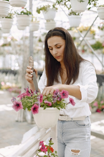 若いブルネットの女性は、庭のホースで鉢植えの植物の世話をします。白いブラウスを着ている女性