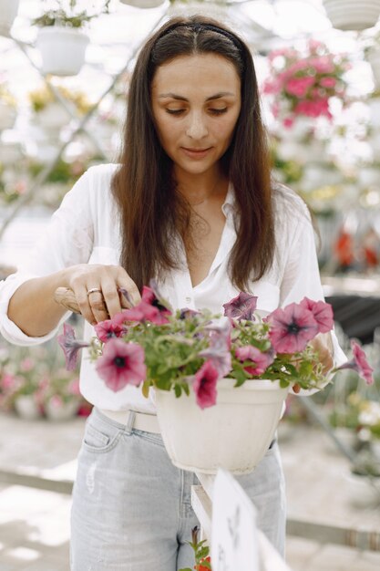 若いブルネットの女性は、庭のホースで鉢植えの植物の世話をします。白いブラウスを着ている女性