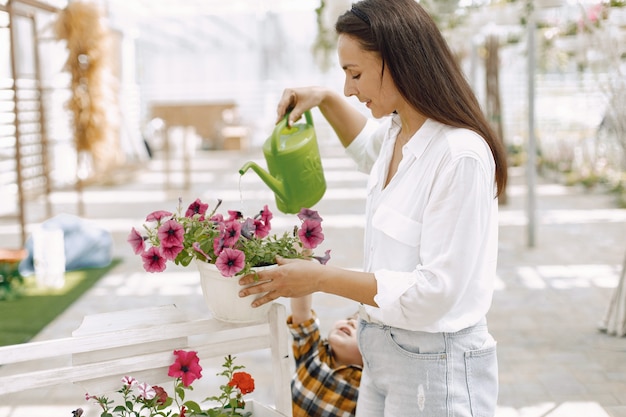 Gardenhose에 화분에 물을 젊은 갈색 머리 여자. 흰 블라우스를 입은 여성