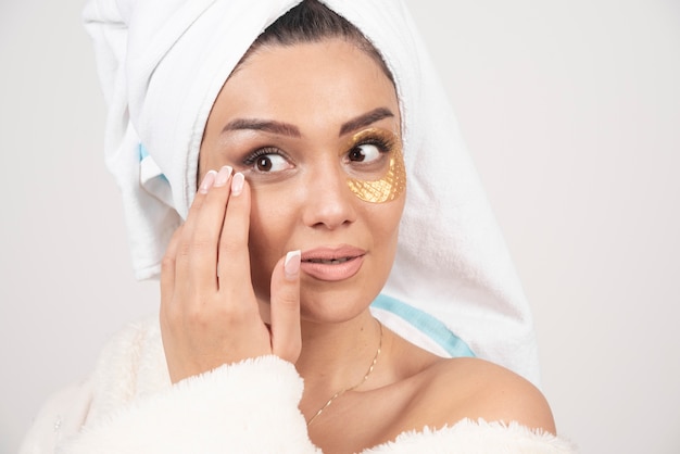 Young brunette woman wearing bathrobe with cosmetic eye patches .