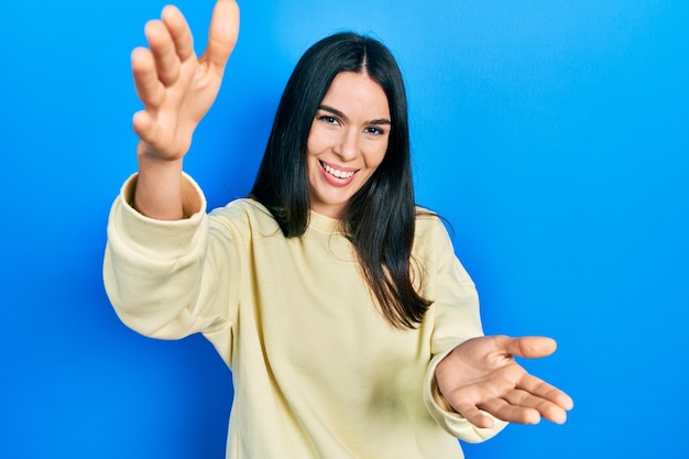 Free photo young brunette woman wearing casual sweatshirt looking at the camera smiling with open arms for hug. cheerful expression embracing happiness.