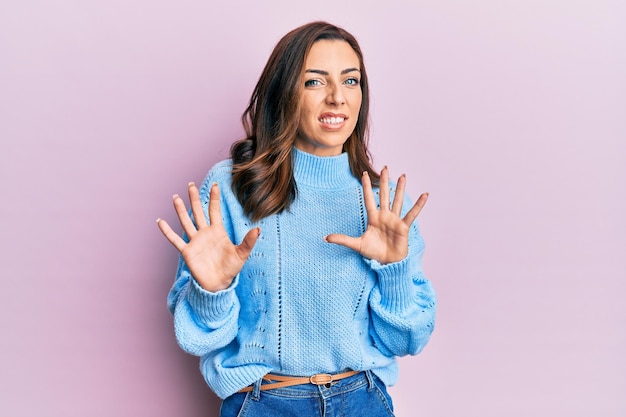 Free photo young brunette woman wearing casual winter sweater over pink background disgusted expression, displeased and fearful doing disgust face because aversion reaction. with hands raised