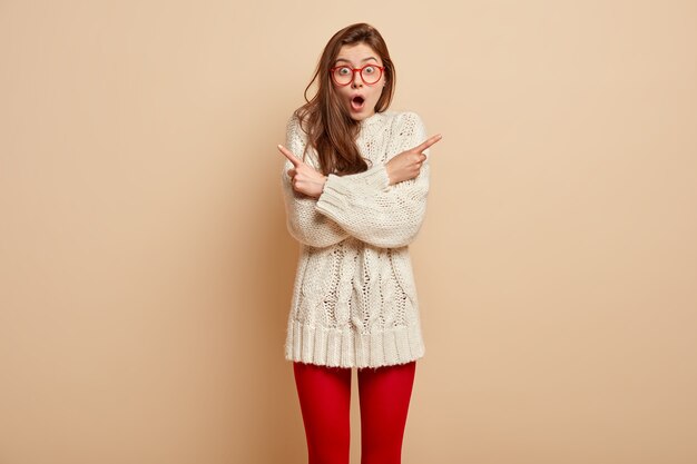 赤い眼鏡と白いセーターを着ている若いブルネットの女性
