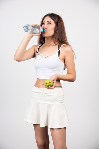 Young brunette woman wearing sportswear with an apple drinking water. 