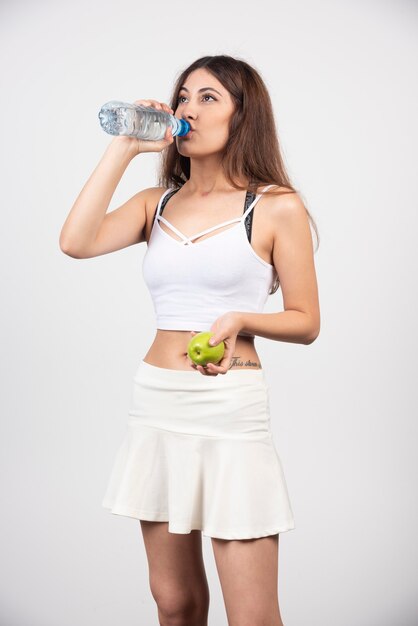 リンゴの飲料水とスポーツウェアを着ている若いブルネットの女性。
