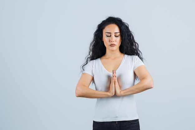 Young brunette woman in a white t-shirt praying