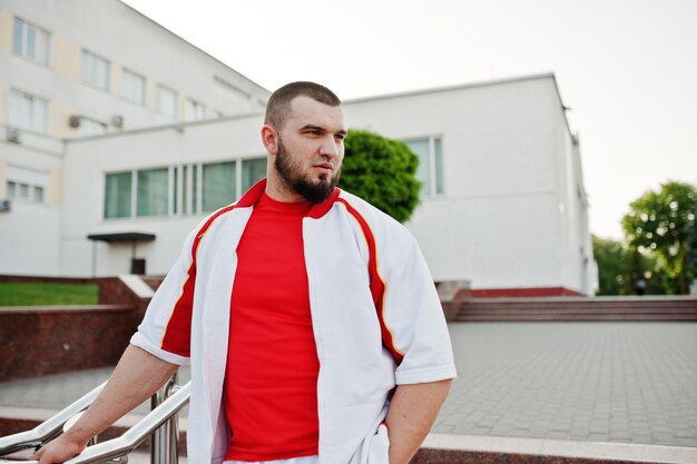 젊은 잔인한 수염된 근육 질의 남자는 빨간 셔츠와 흰색 스포츠 정장에 착용