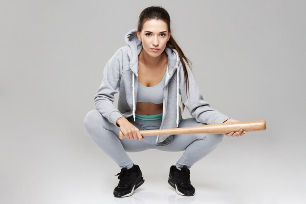 Young brutal sportive woman in sportswear sitting with bit on white.