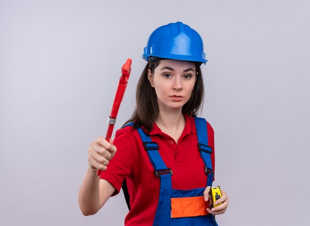 Young builder girl holds pipe wrench and tape measure on isolated white background with copy space