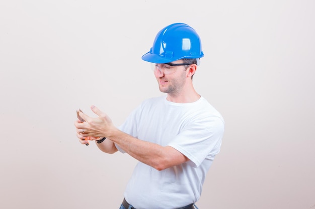 Free photo young builder having finger with pliers in t-shirt, helmet and looking amused