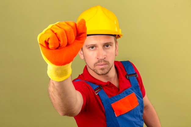 Free photo young builder man in construction uniform gloves and safety helmet knocking at fictitious door or window over isolated green wall