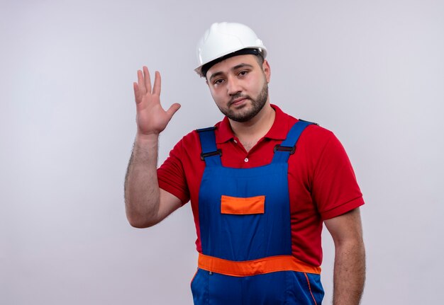 Young builder man in construction uniform and safety helmet looking at camera with raised arms looking confident 