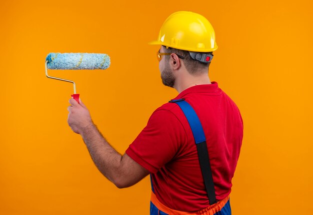 Young builder man in construction uniform and safety helmet  with his back holding paint roler