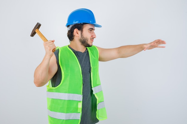 Young builder man getting ready to using hammer in workwear uniform and looking confident , front view.